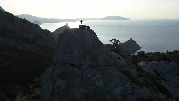 Dynamic Flight Around a Girl Standing on the Top of a Mountain Over the Sea at Sunrise. Flight Over