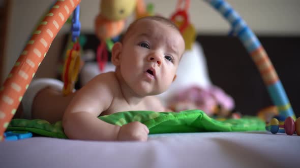 Newborn Baby Lies on Its Tummy on a Play Mat and Yawns