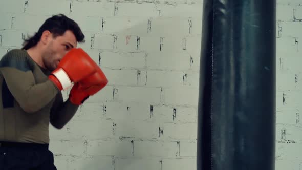 Boxer Man in Gloves Training Kick By Boxing Bag on White Brick Wall Background