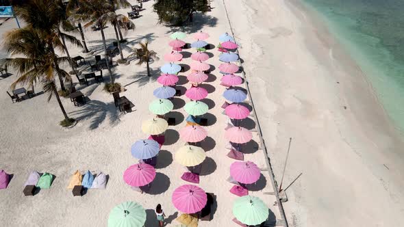 Aerial fly over multicolored umbrellas on golden beach beside tropical ocean shore on Gili Trawangan