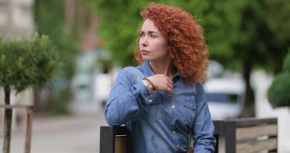 Attractive Young Ginger Woman Sitting on a Bench Looking Away and at the Camera, Beautiful Face
