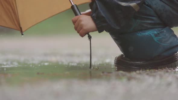 SLOW MOTION, CLOSEUP - A child jumping in the puddle during heavy rain