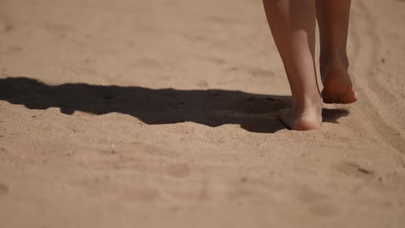 Woman is Walking on Sand Strolling on Beach in Summer Closeup of Bare Feet