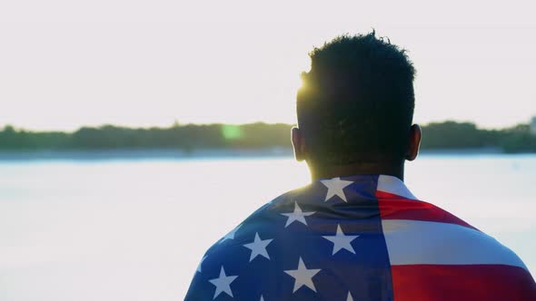 Afroamerican Man with American Flag on Shoulders Looks Into Distance at Sunrise