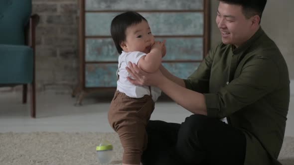 Asian young father in bright living room playing on floor with his young son