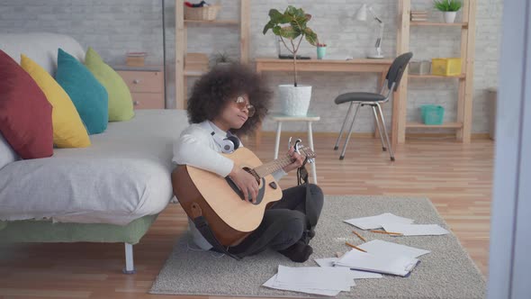 African American Woman with an Afro Hairstyle Plays Guitar Sitting on the Floor