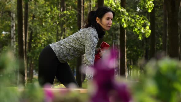 Young Attractive Sportive Woman Practicing with Dumbbell Outdoors