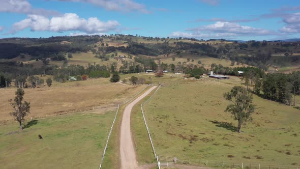 Aerial footage of a dirt road with white fence running through a green farming field