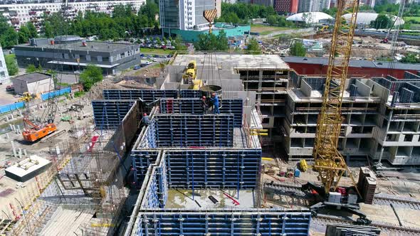 A drone moves from construction workers pouring cement into blue formwork