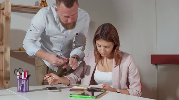 Woman Is Consulting with Her Manager in Office He Is Drawing in Her Notebook