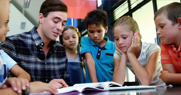 Kids listening to teacher while reading book in classroom