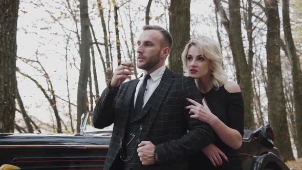 Portrait of Elegant Lady Leans on Her Man Smokes Cigar in Forest