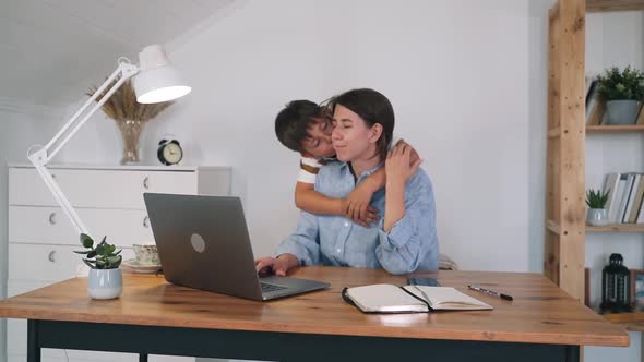 A Woman with a Child is Working at a Laptop
