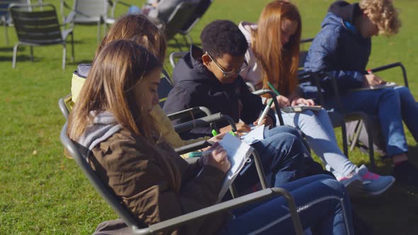 Diverse Preteen Schoolchildren Sitting on Folded Chairs at Outdoors Lesson in Park and Painting Mask