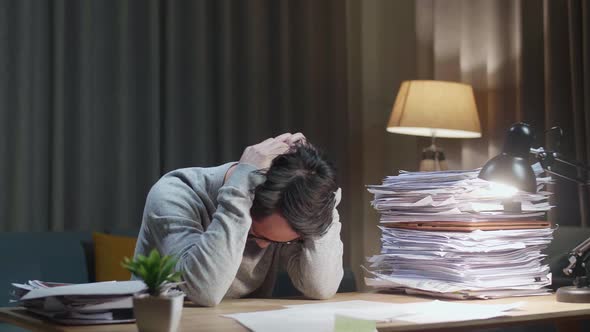 Asian Man Throwing Paper And Having Headache While Working Hard With Documents At Home