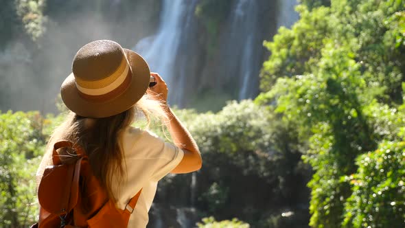 Back View of Woman with Photo Camera Shooting Tropical Waterfall