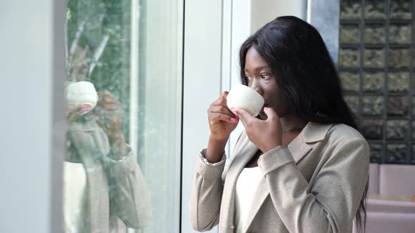 AfricanAmerican Woman Drinks Coffee Near Window in Office