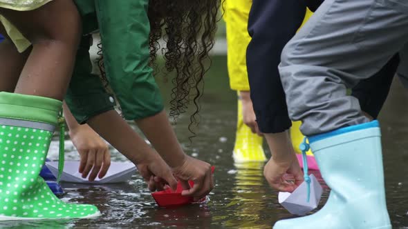 Children Putting Paper Boats in Puddle