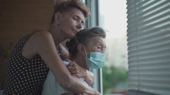 Lonely Senior Woman 90 Years Old in Medical Mask and Her Mature Daughter Standing in Embrace Looking