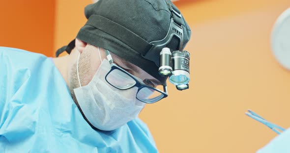 Closeup Face of Male Veterinarian in Glasses Cap and in Surgical Outfit While He is Operating the