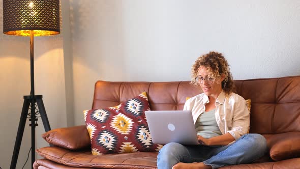 Modern woman sitting on the couch and use laptop computer for work or surf the web - Adult online