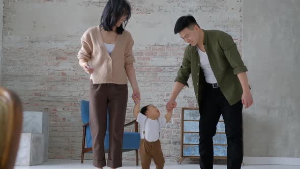 First step. Loving young parents hold hands of an innocent baby inside the room