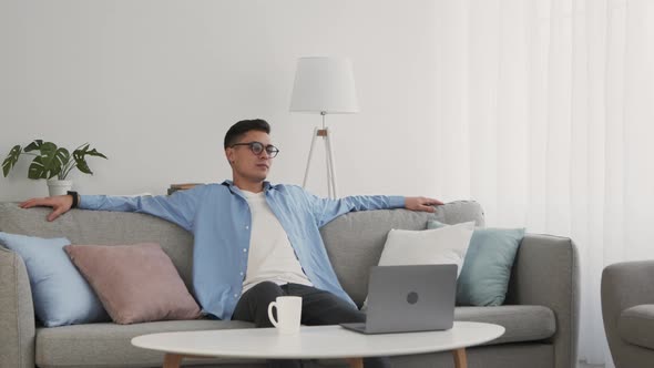 Young Man in Glasses Sitting on Couch Taking Break in Online Work at Home Slow Motion