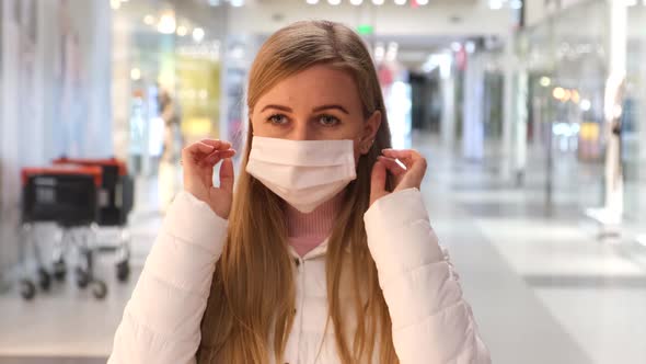 Blonde woman puts on a medical mask in a grocery supermarket and looks at the camera