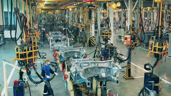 Car Workers Moving a Car Body Using Chains on an Assembly Line