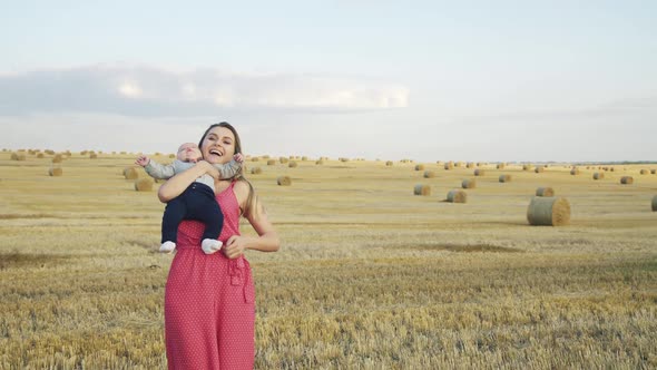 Happy Mother Rejoices in the Haystack Field When Caresses and Kisses Cute Baby