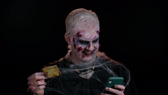 Sinister Man Halloween Zombie Using Credit Bank Card and Smartphone While Purchases Online Shopping