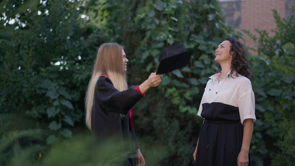 Excited Grad Woman Throwing Graduation Cap Up in Slow Motion with Cheerful Mother Smiling Clapping