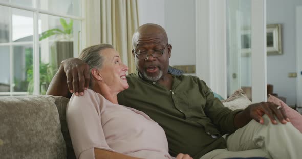 Happy senior diverse couple wearing shirts and watching tv in living room