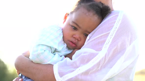 close up shot of a small South African girl falling asleep in her mother's arms with sun in the back