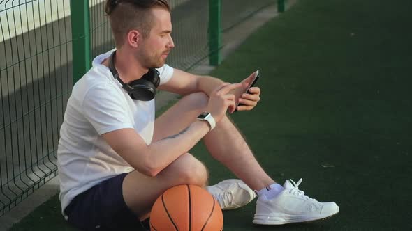 Relax After Streetball Training on Court Man is Surfing Internet By Smartphone