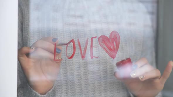 Female Hand Draws Red Heart Word LOVE on the Window with Paint