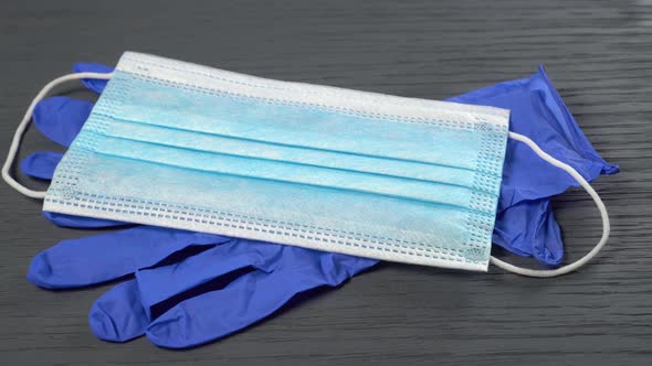 Disposable protective medical mask and blue nitrile gloves on a gray wooden background.