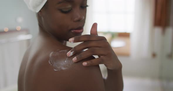 Portrait of african american attractive woman applying body balm in bathroom