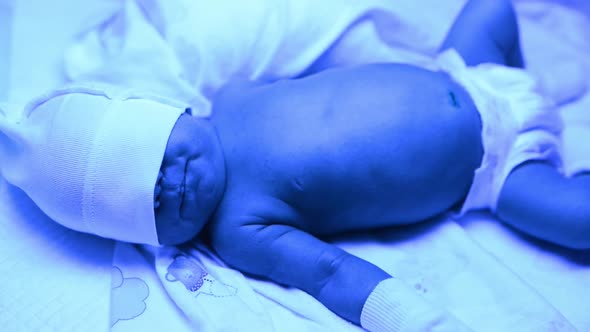 Newborn Having a Treatment for Jaundice Under Ultraviolet Lamp in Home Bed