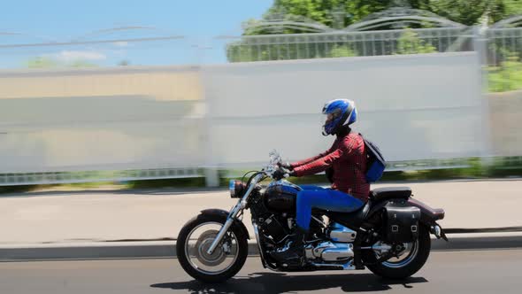 Biker in Red Shirt and Blue Helmet in Jeans Drives His Brown Dragster Down Road Through City