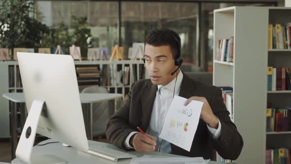 Bussinesman Working Through Documents on His Computer and Shows Paperwork Statistics in Online Video