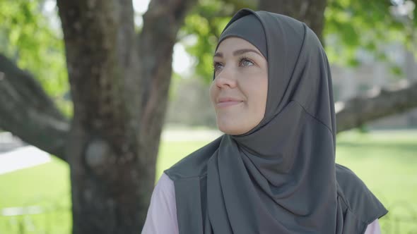 Close-up Face of Charming Muslim Woman in Traditional Grey Hijab Enjoying Sunny Day Outdoors