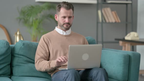 Man with Laptop Reacting to Loss on Sofa