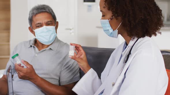 Mixed race female doctor and senior man wearing masks and holding pills