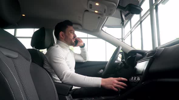 Businessman is Talking on the Phone in Car Showroom Sitting in a New Car