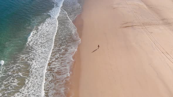 One person walking alone on golden beach at Porto Santo island, Portugal. Aerial tilt-up