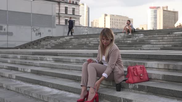 A business woman sits on the stairs and massages her tired legs.