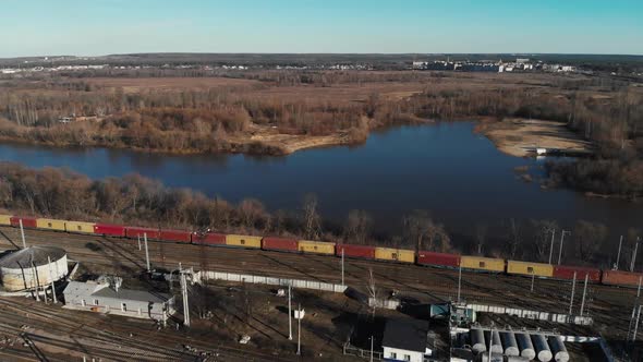 Aerial View of a Large Train on the Rails Next To the River. The Camera Flies Up To a Long Freight