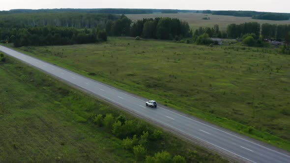 Aerial View of a Car Driving Along the Road Among Fields of Green Grass