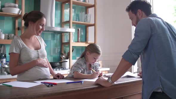 Expectant parents watching as young daughter colors in the kitchen